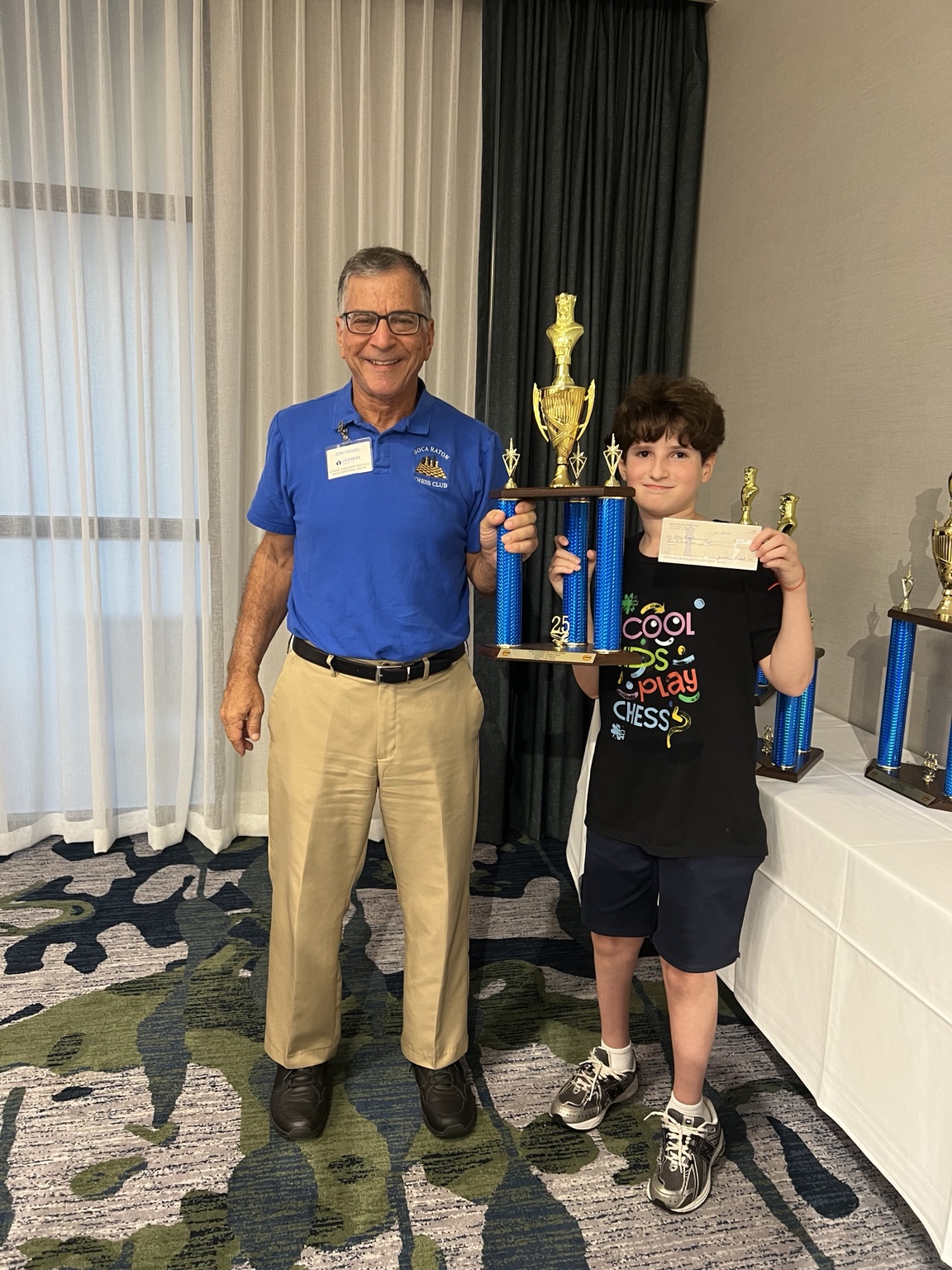 Chess coach with a student holding a tournament trophy